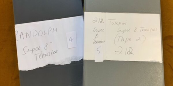 A close-up of two grey video tape cases, large white labels on their front identifying the contents as 'Turpin Super 8 Transfers'.