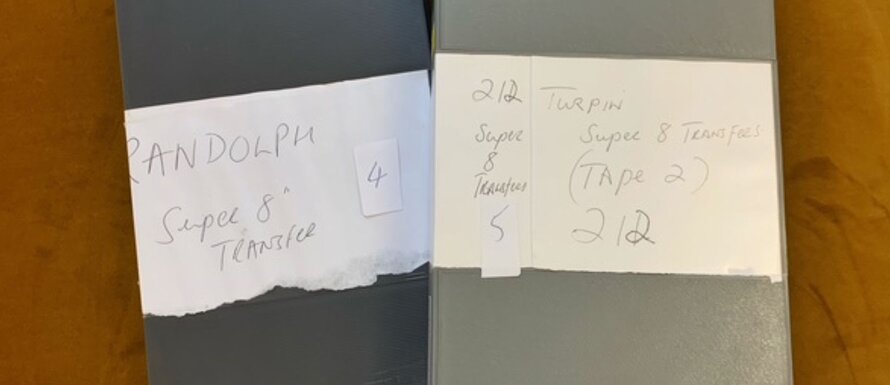 A close-up of two grey video tape cases, large white labels on their front identifying the contents as 'Turpin Super 8 Transfers'.
