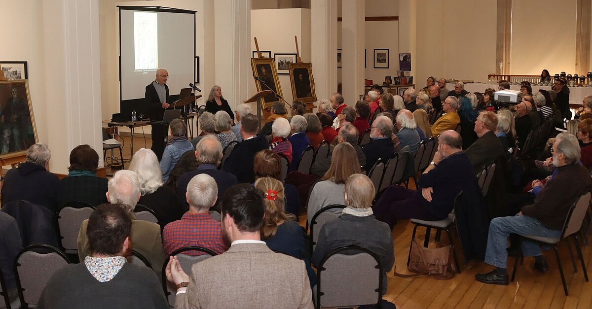 Cynulleidfa'n gwrando ar gyflwyniad gan ddau berson yn Oriel Gregynog