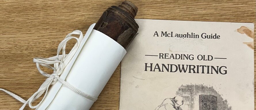 Image of a scroll wrapped in paper and tied with string, next to the cover of a volume bearing the title 'Reading Old Handwriting'