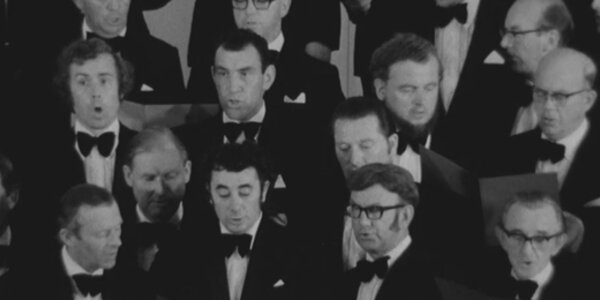 [Translate to Cymraeg:] A black and white image showing members of a male voice choir singing.
