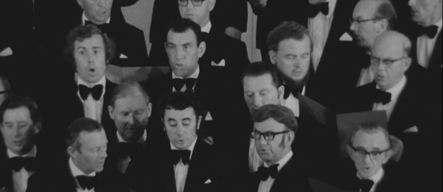 [Translate to Cymraeg:] A black and white image showing members of a male voice choir singing.